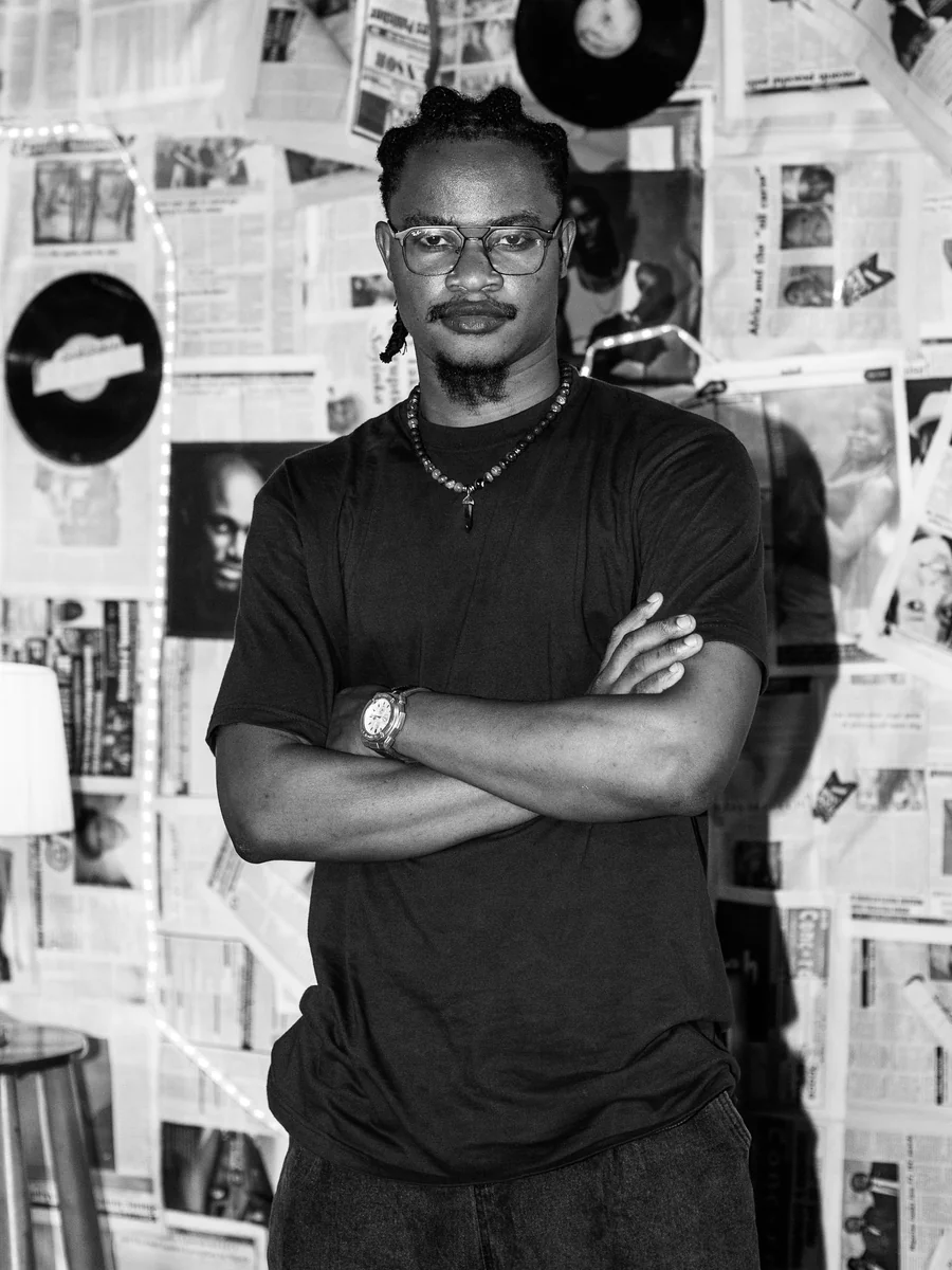 DJ Bhig Wheelz posing with folded arms in a record-themed room