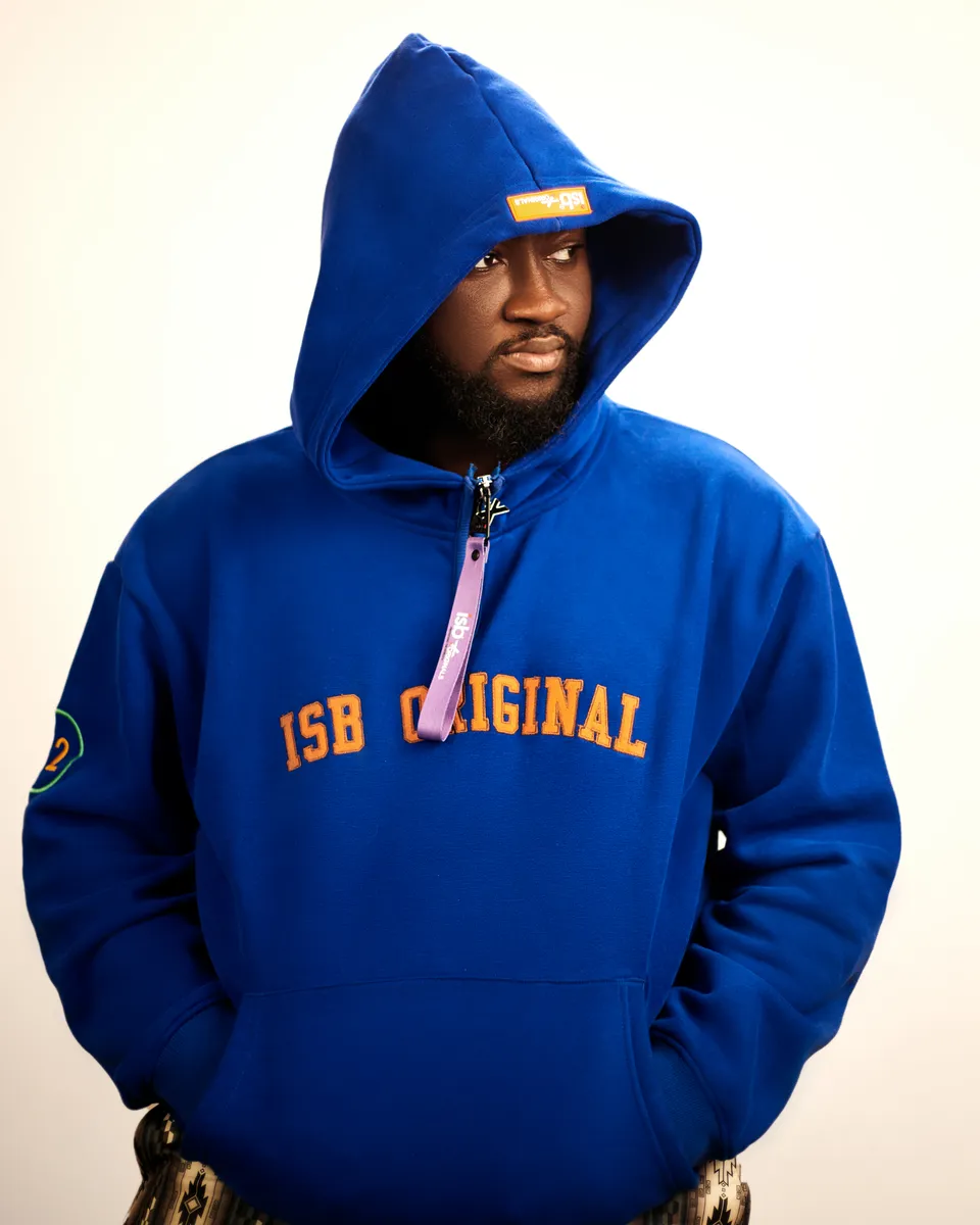 Bigg Clemm in a blue hoodie, hands in pockets, against a bright backdrop