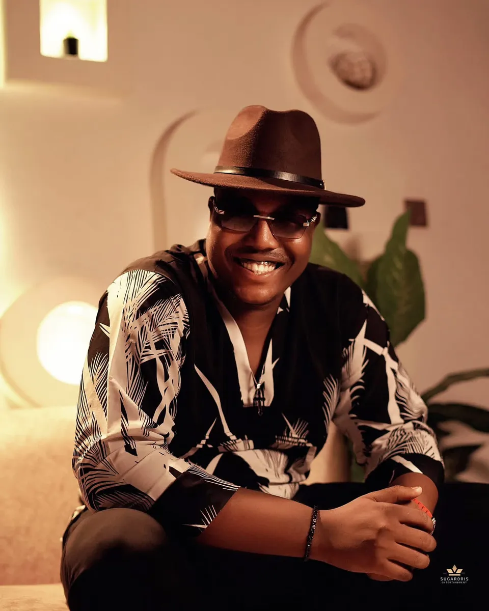 Joe D Virus smiling in sunglasses and a brown hat under warm indoor lighting