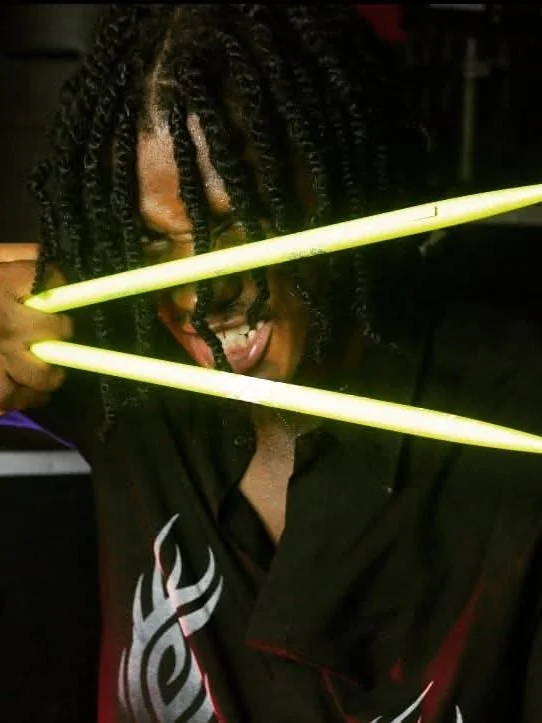 DJ Knackademus holding glowing drumsticks in a dark room