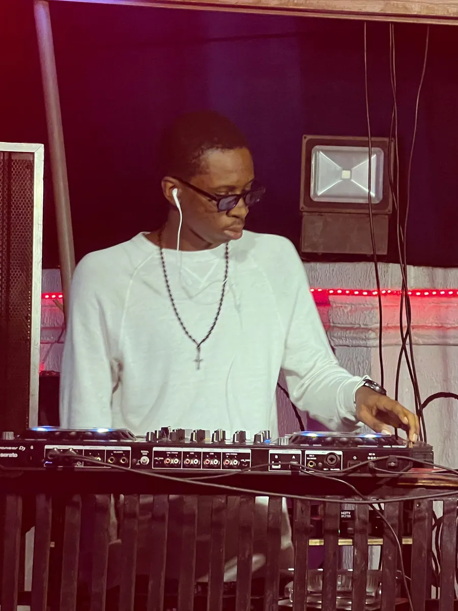 Raey DJing in a white shirt and sunglasses at a club performance