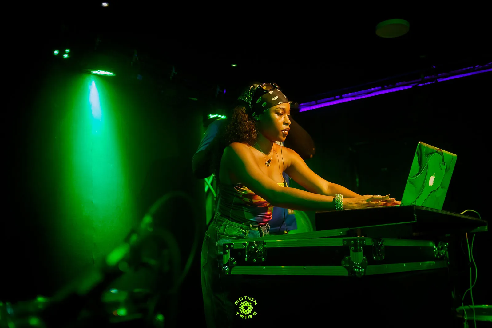 Woman DJ works at a laptop and decks beneath a green spotlight