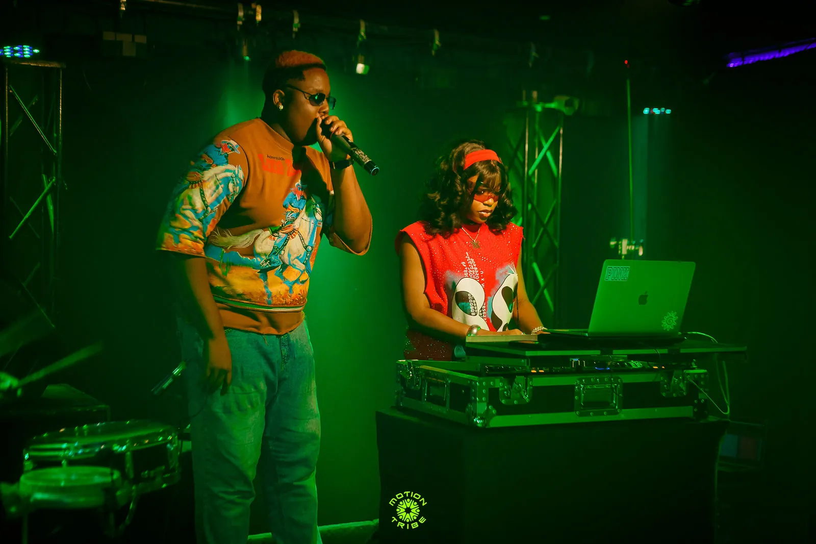 Vocalist sings into a microphone while a DJ performs behind him