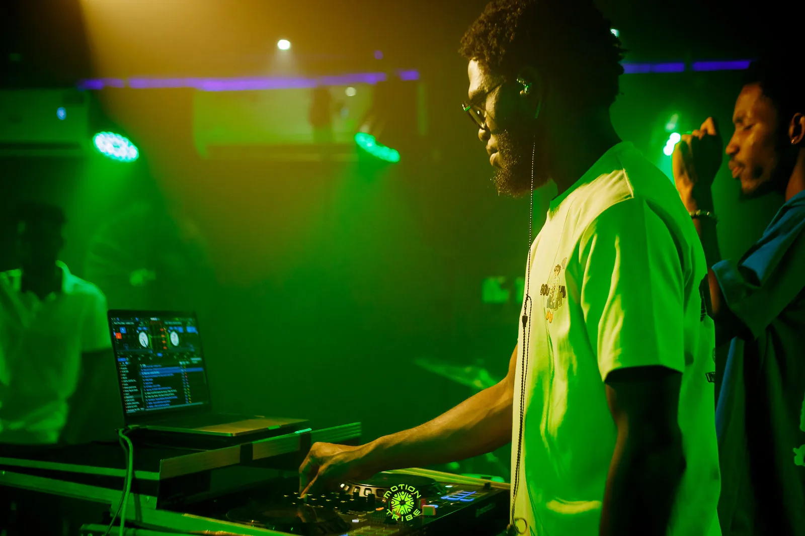 DJ in a white shirt performs at a mixer under green stage lights