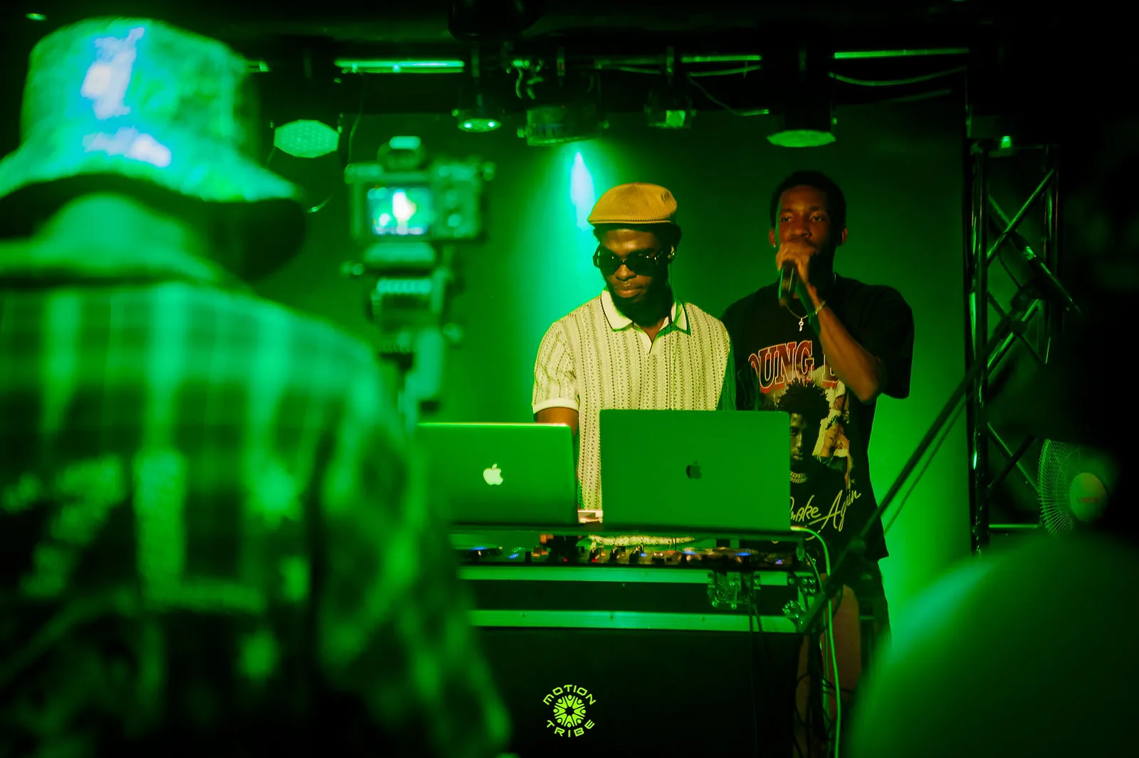 DJ performs behind a laptop and decks as a blurred dancer fills the foreground