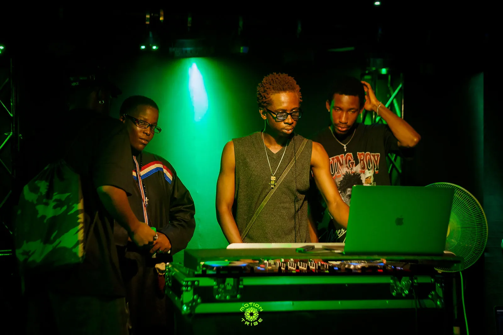 Three people perform at a DJ booth under vivid green stage lighting