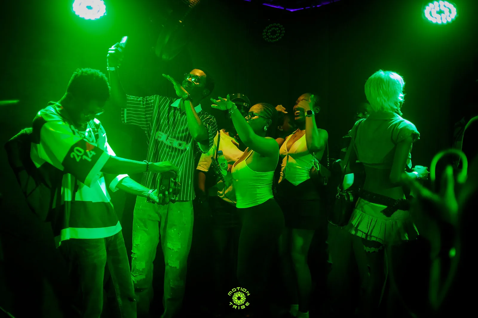 Ravers dance together beneath vivid green club lighting