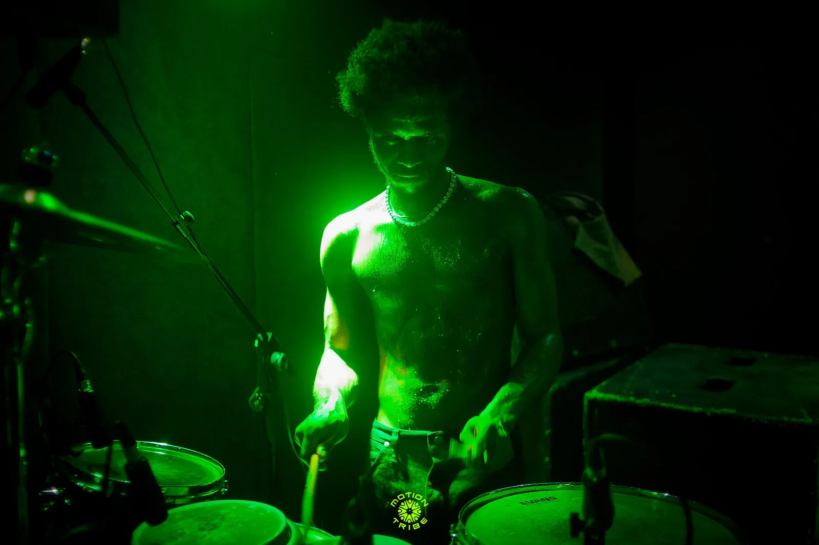 Drummer performs beside his kit under a bright green spotlight