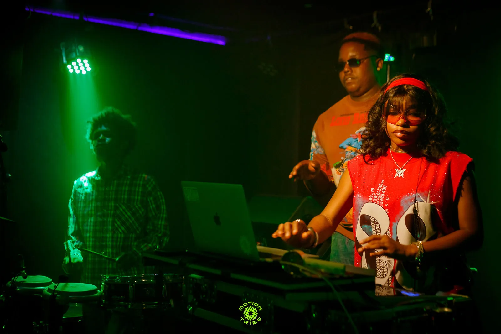 Woman in a red shirt performs at DJ decks with a laptop behind her
