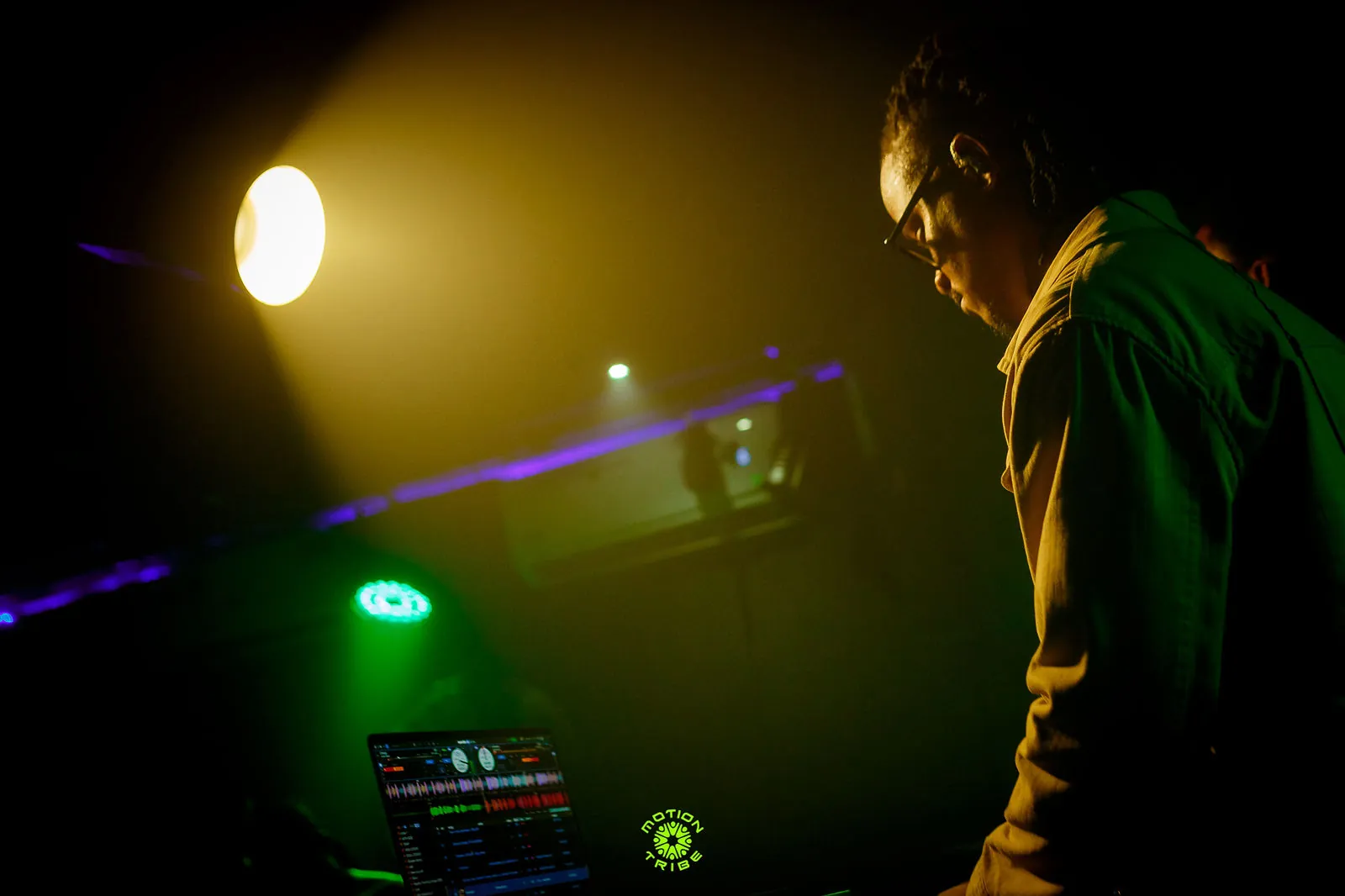 DJ works at a laptop beneath a warm spotlight and purple stage lights